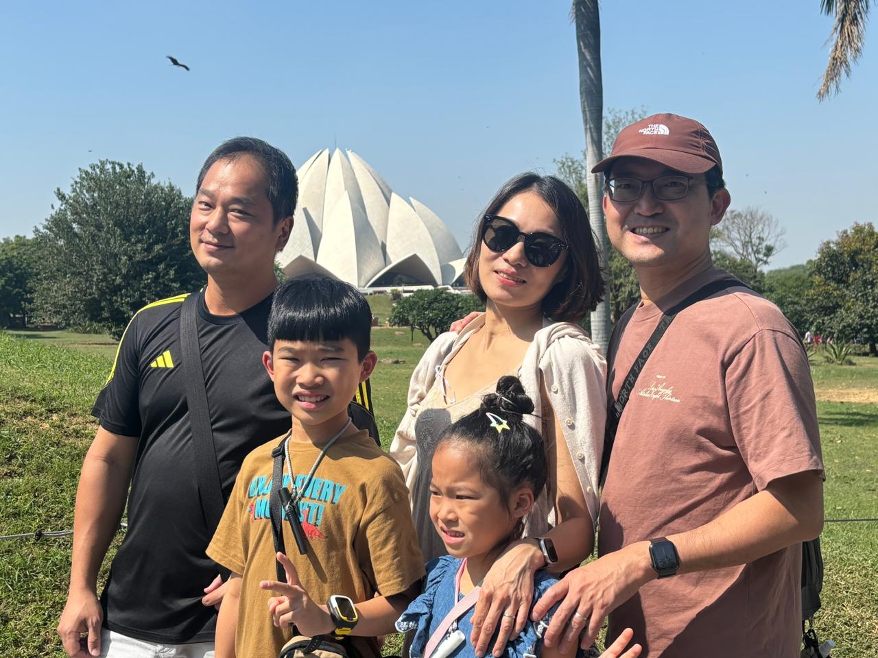 A group of adults and children posing in front of the Lotus Temple in Delhi during a Delhi Tour and Golden Triangle Tour.