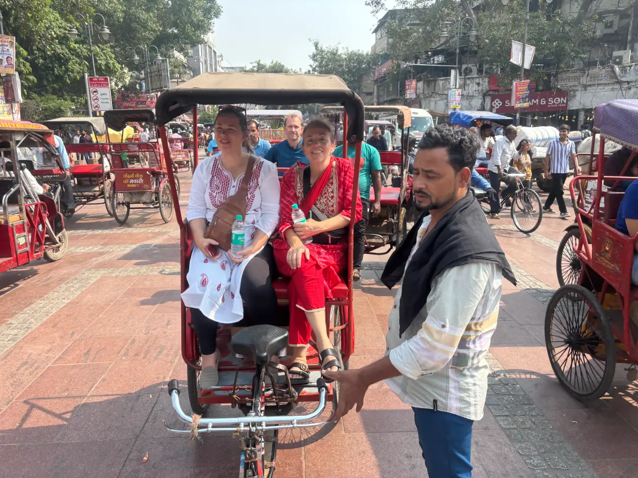 Two tourists seated in a cycle rickshaw while the driver pulls them through the busy Chandni Chowk market in Old Delhi during a Golden Triangle tour