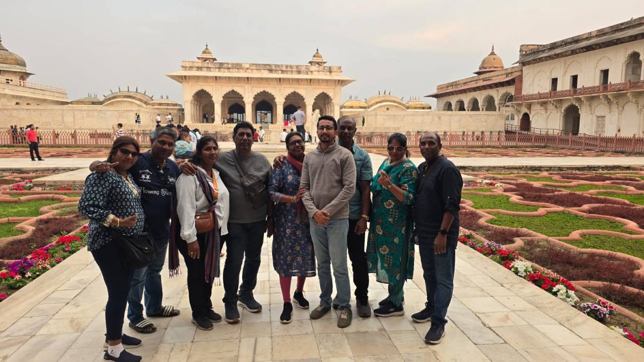 Eight tourists standing together at Angoori Bagh inside Agra Fort, with Jahangir Mahal Mughal architecture in the background during a guided tour by Agra Trip Packages.