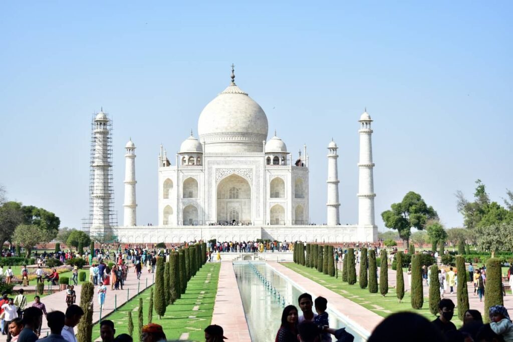 Front view of the Taj Mahal with the reflecting pool, Charbagh gardens, visitors, and one minaret under restoration in Agra, India.