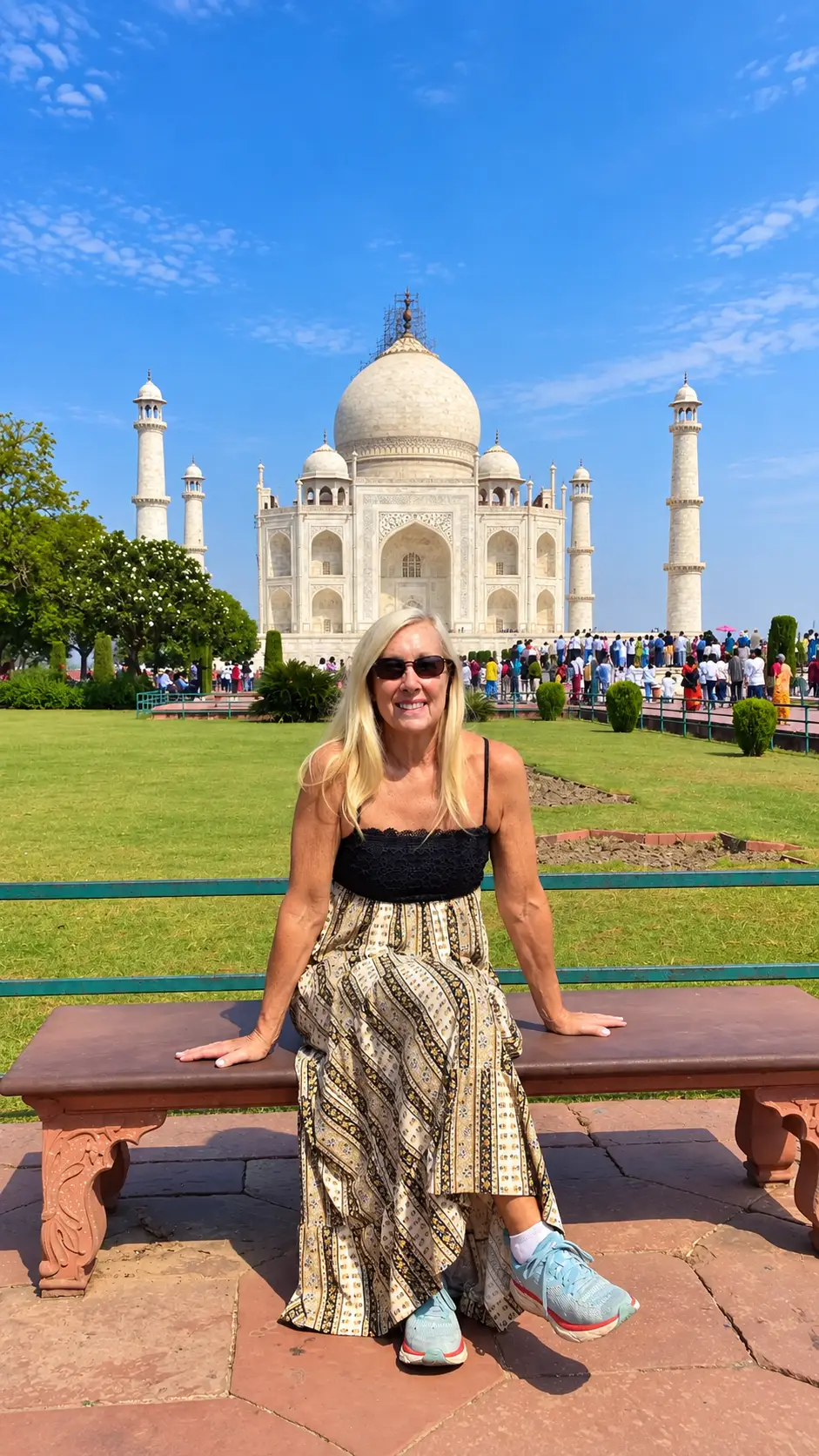 Female tourist sitting on a bench in the Taj Mahal gardens with the monument in the background in Agra, India.