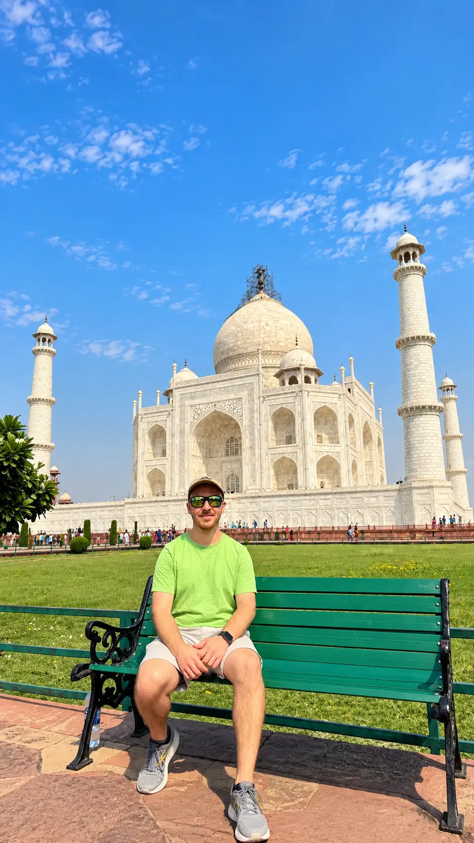 Male tourist sitting on a green bench with the Taj Mahal in the background in Agra, India.