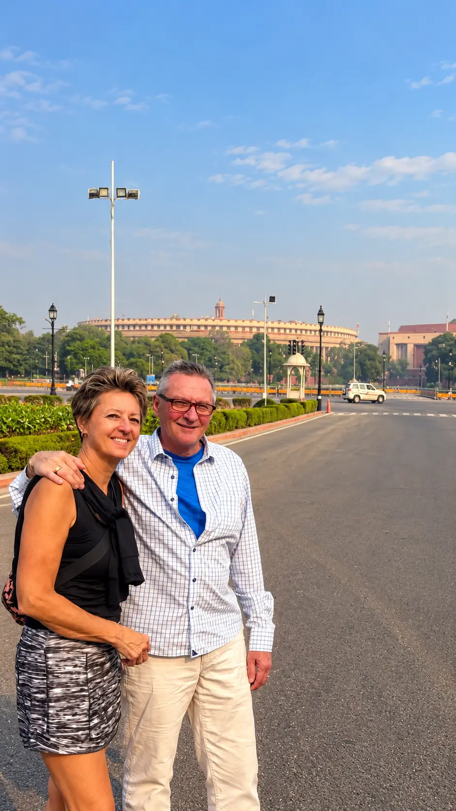 Tourist couple posing on a New Delhi avenue with Parliament House in the background.