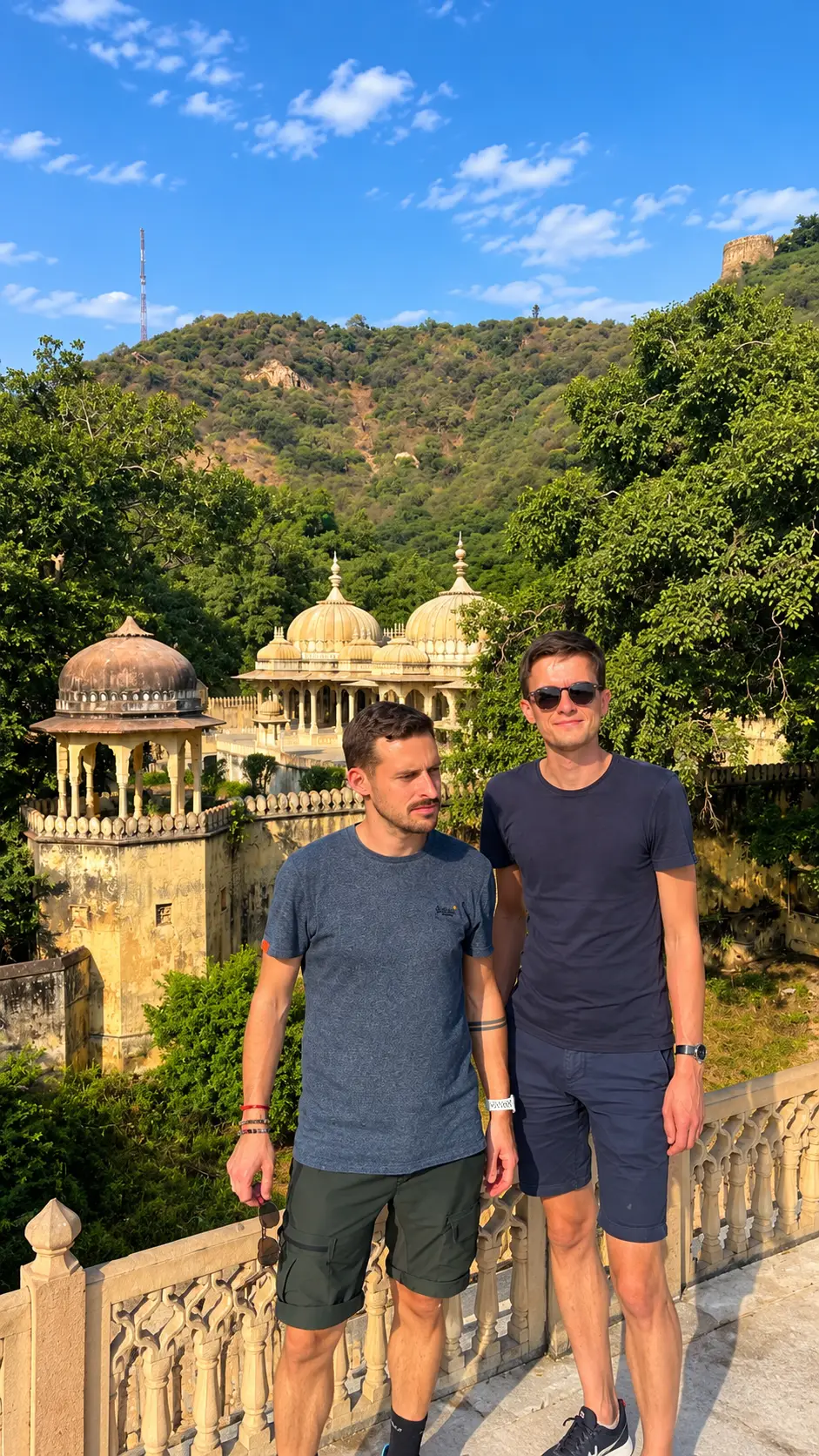 Two foreign male tourists posing at Ranthambore Fort with forested hills in Ranthambore National Park behind them.