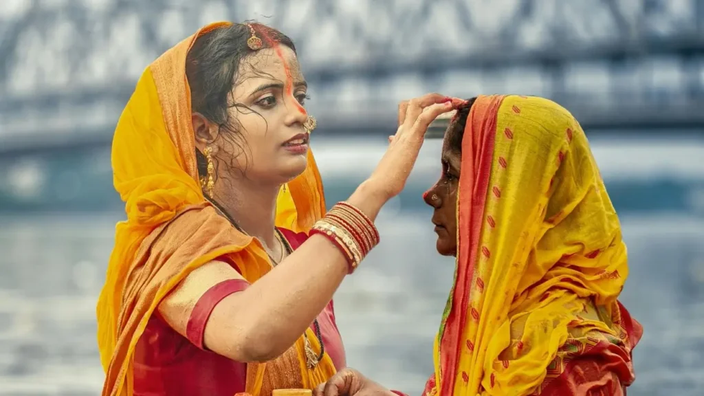 A woman in traditional Indian attire applies a ceremonial tilak to another woman during a Hindu religious ritual, symbolizing devotion, blessings, and India's vibrant cultural traditions.