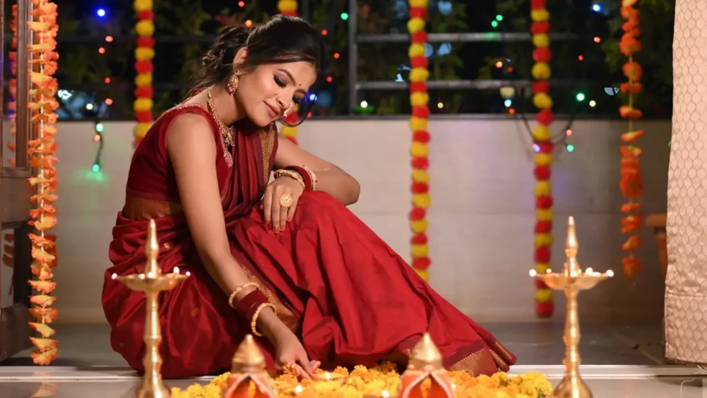 A woman in a traditional red saree lighting diyas and decorating with marigold flowers during Diwali, celebrating India's Festival of Lights and cultural traditions.