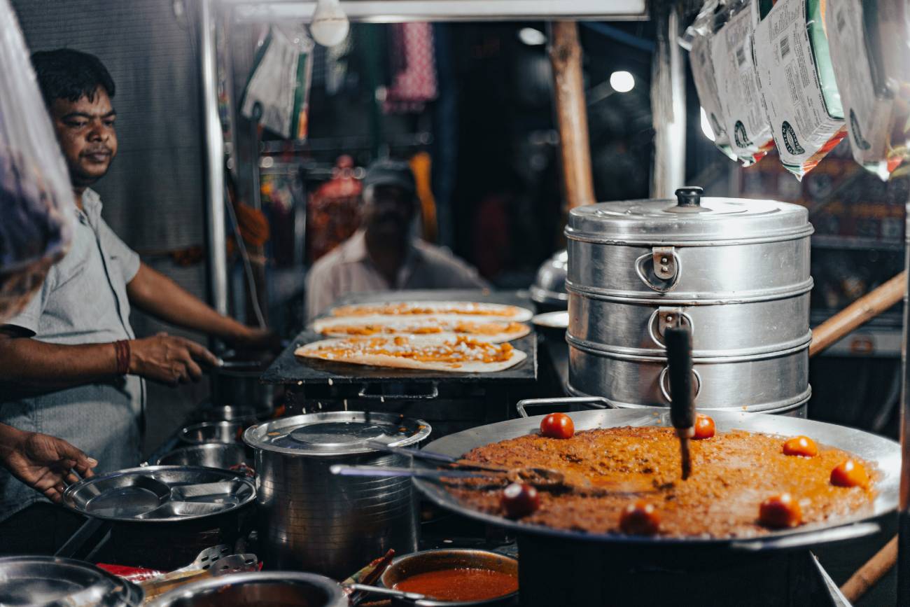 Explore North India’s Most Iconic Wonders 90 Street food vendor cooking traditional Indian food at a busy local market stall in Agra with large cooking pots, fresh flatbreads, and authentic evening food scene.