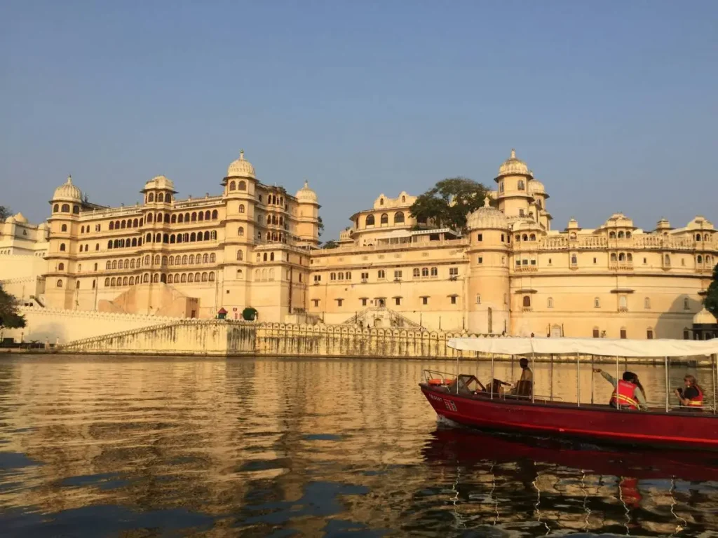 Boat sailing on Lake Pichola with the City Palace overlooking the water in Udaipur, Rajasthan, India.